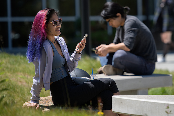 Student sitting outside on campus using her phone